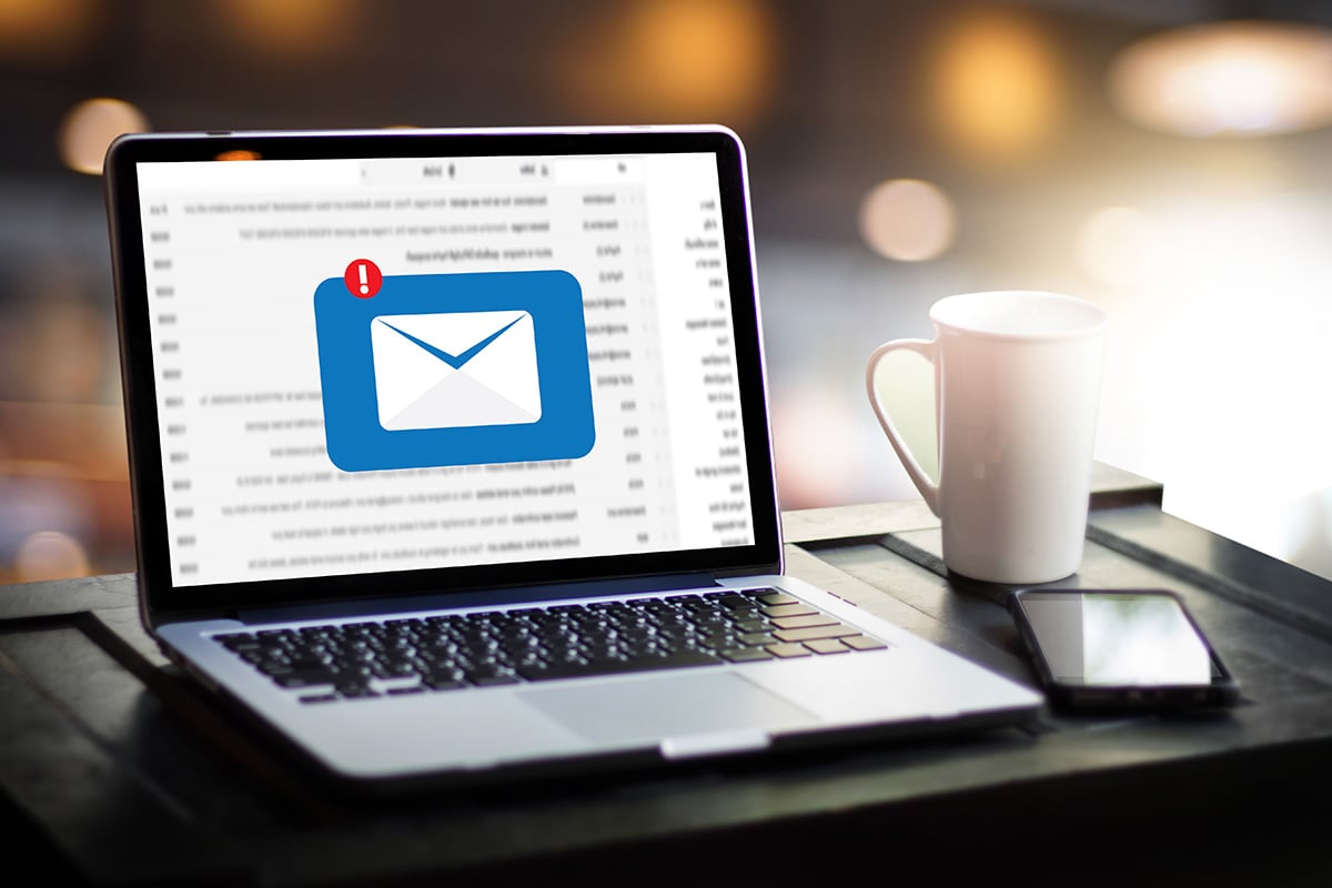 Email list on laptop displayed on a desk next to a cup of coffee